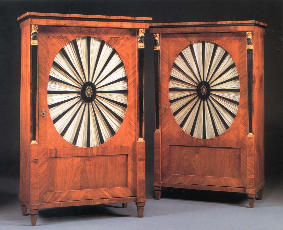 19th Century AUSTRIAN, Pair of Biedermeier Gilt-Metal-Mounted Black Walnut, Ebonized and Parcel Gilt Cabinets, 1800-1825
Mixed woods, 66 1/2 x 40 1/8 x 21 in. (168.9 x 101.9 x 53.3 cm)
Each with a molded cornice above the cabinet door centered by an oval, glazed panel with radiating ebonized splats centered by a pierced oval mount opening to reveal shelves, flanked by military terminal supports raised on square tapering feet, now fitted with silk fabric.
BIE-002-FU